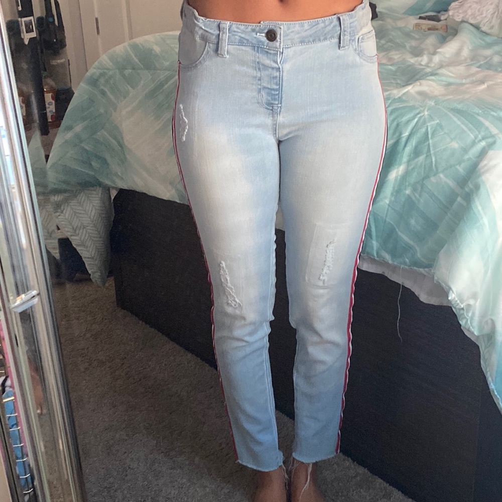 Denim jeans with small rips and pink, white, and navy blue stripes down the side